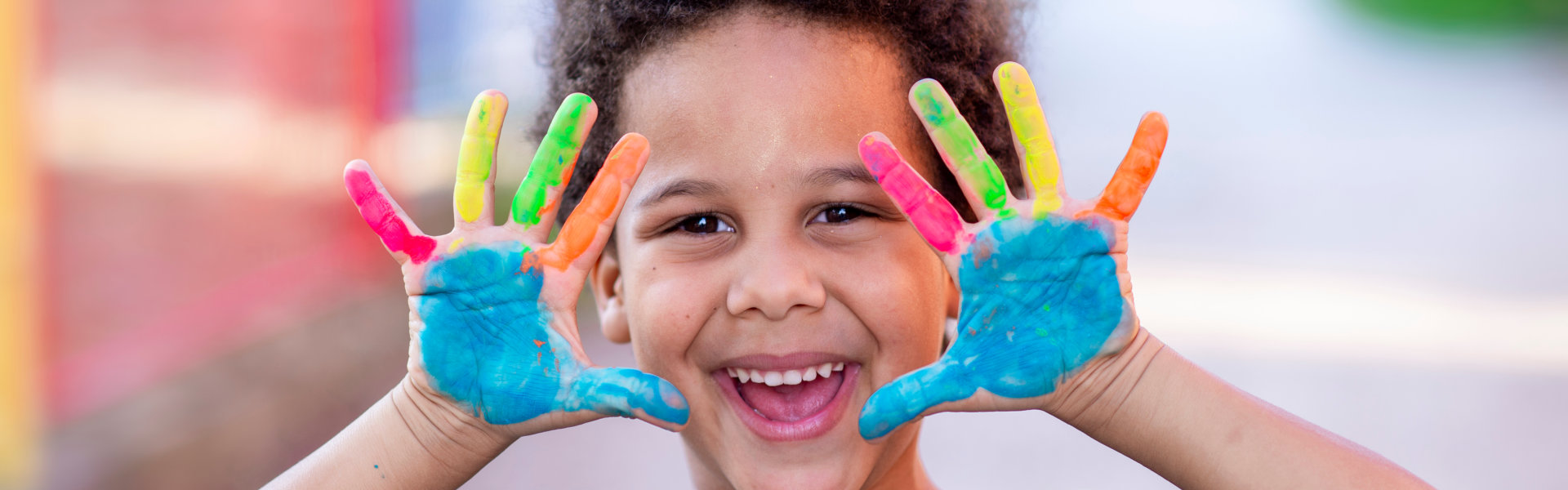 boy smiling while raising his hands full of paint